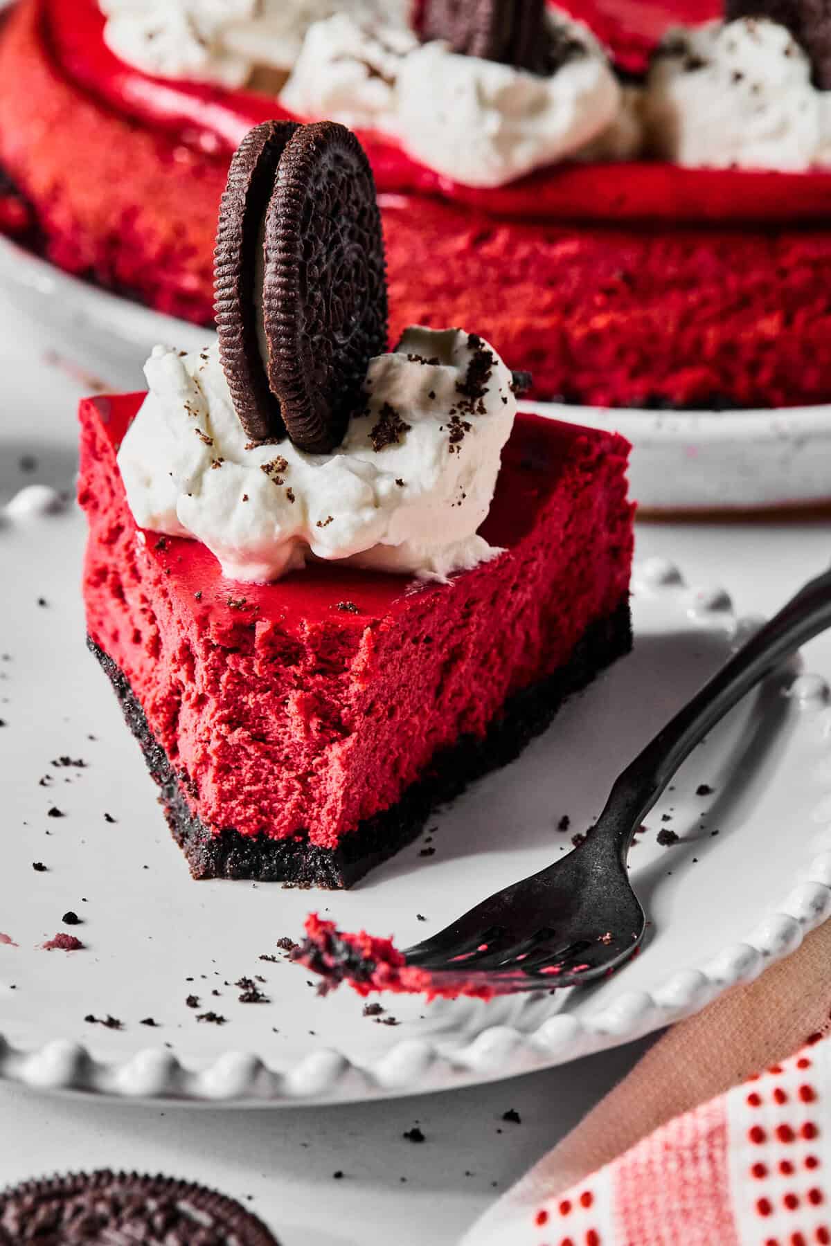 A piece of red velvet cheesecake with a bite missing next to a dirty fork on a white plate.