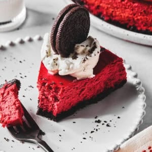 A slice of red velvet cheesecake with a bite on a fork all on a white plate.