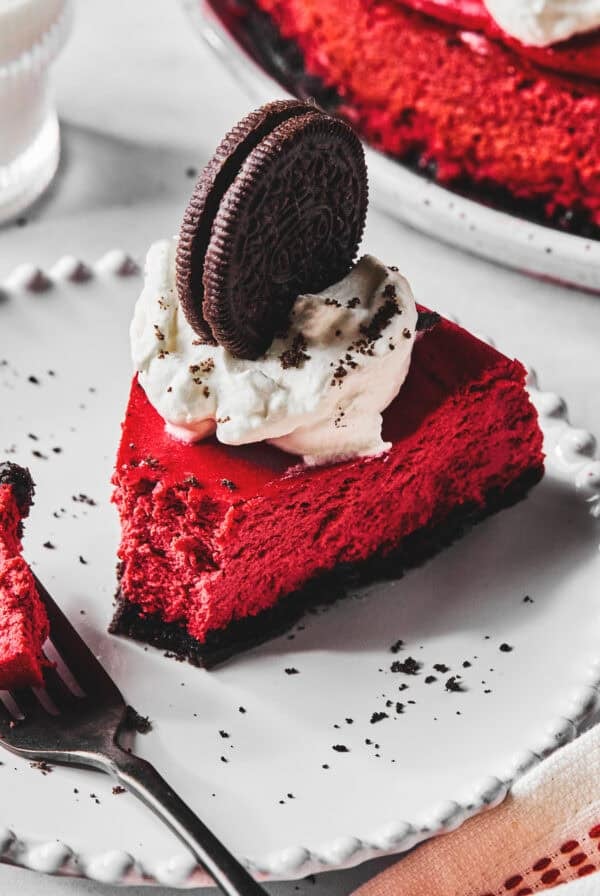 Close up of a slice of red velvet cheesecake with a bite on a fork all on a white plate.