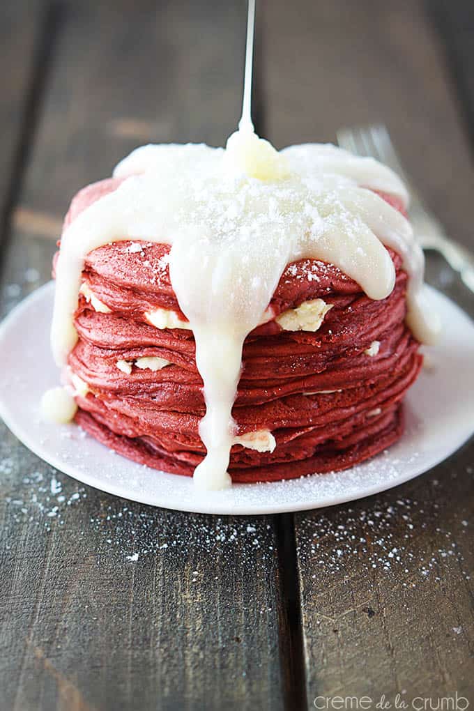 red velvet cheesecake pancakes on a plate with cream cheese icing being poured on top.