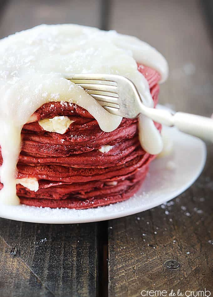 red velvet cheesecake pancakes with cream cheese icing on a plate with a fork taking a bite.