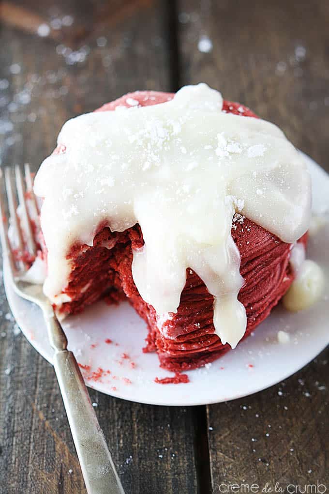 red velvet cheesecake pancakes with cream cheese icing on a plate with a bite missing and a dirty fork on the side.