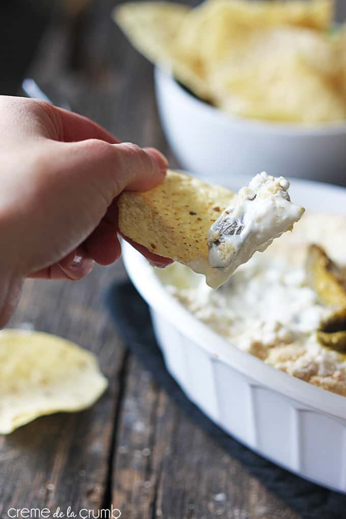 a hand holding a chip with skinny Jalapeño popper dip on it with the rest of the dip in a serving bowl faded in the background.