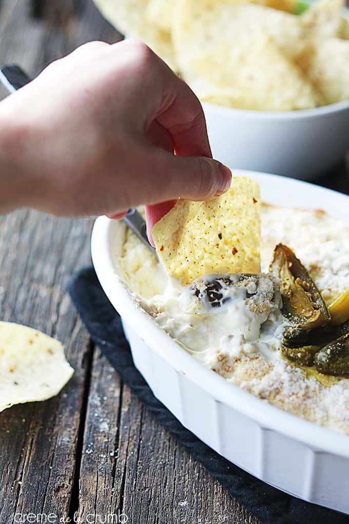 a hand dipping a chip in skinny Jalapeño popper dip in a serving bowl on a table.