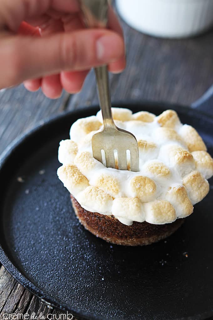 a hand taking a bite out of a S'mores lava cake in a skillet with a fork.