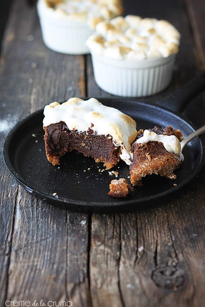 S'mores lava cake in a skillet with a fork on the side with a bite on top with other cakes in dessert bowls faded in the background.