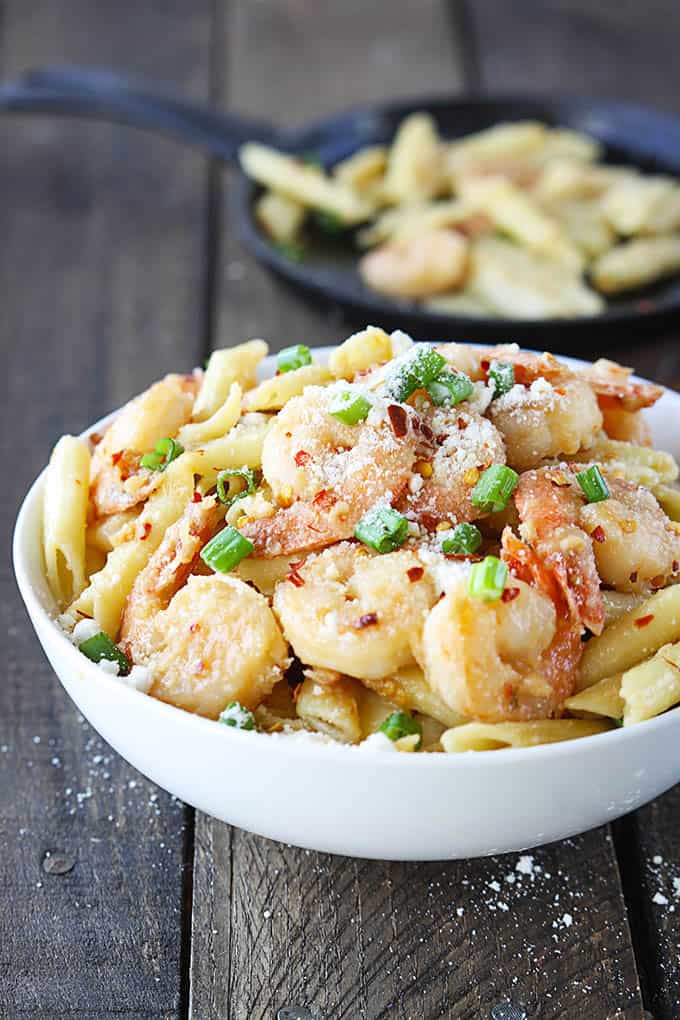 spicy parmesan shrimp pasta in a bowl with a skillet with more pasta faded in the background.