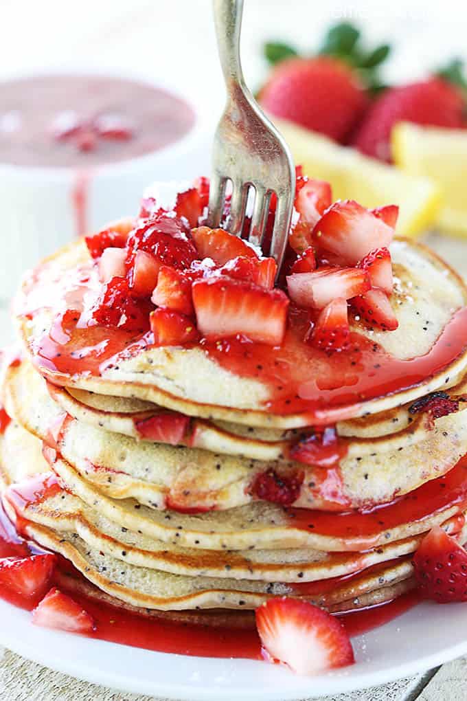 strawberry lemon poppyseed pancakes with strawberry sauce and strawberries and a fork on top on a plate.