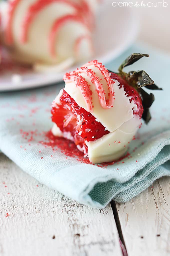 a white chocolate dipped strawberry on a blue cloth napkin with a bite taken from it.