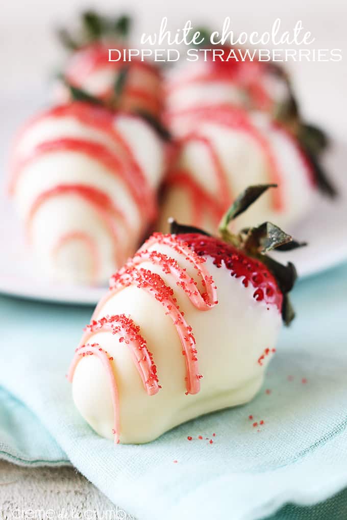 a white chocolate dipped strawberry on a blue cloth napkin with more strawberries on a plate faded in the background with the title of the recipe written on the top right corner of the image.