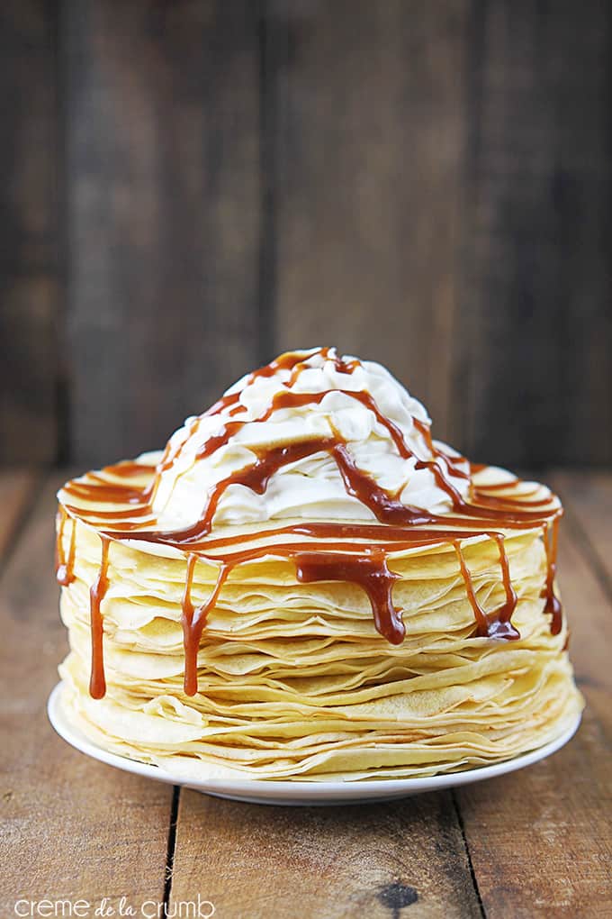 cinnamon roll crepes with cinnamon sauce and whipped cream on top on a plate.