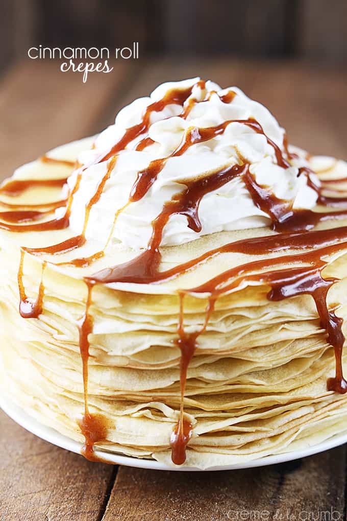 cinnamon roll crepes with cinnamon sauce and whipped cream on top on a plate with the title of the recipe written on the top left corner of the image.