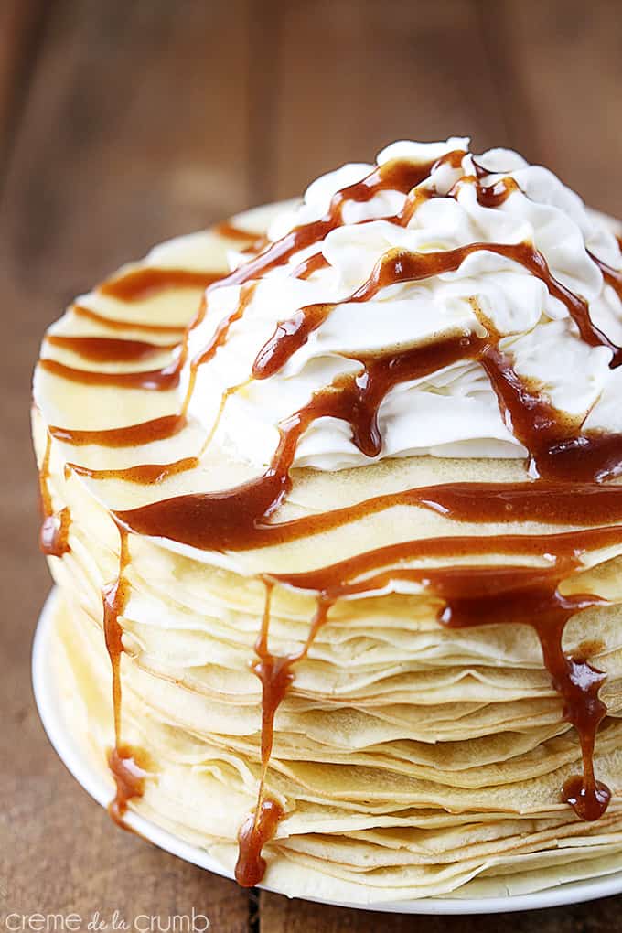 close up of cinnamon roll crepes with cinnamon sauce and whipped cream on top on a plate.