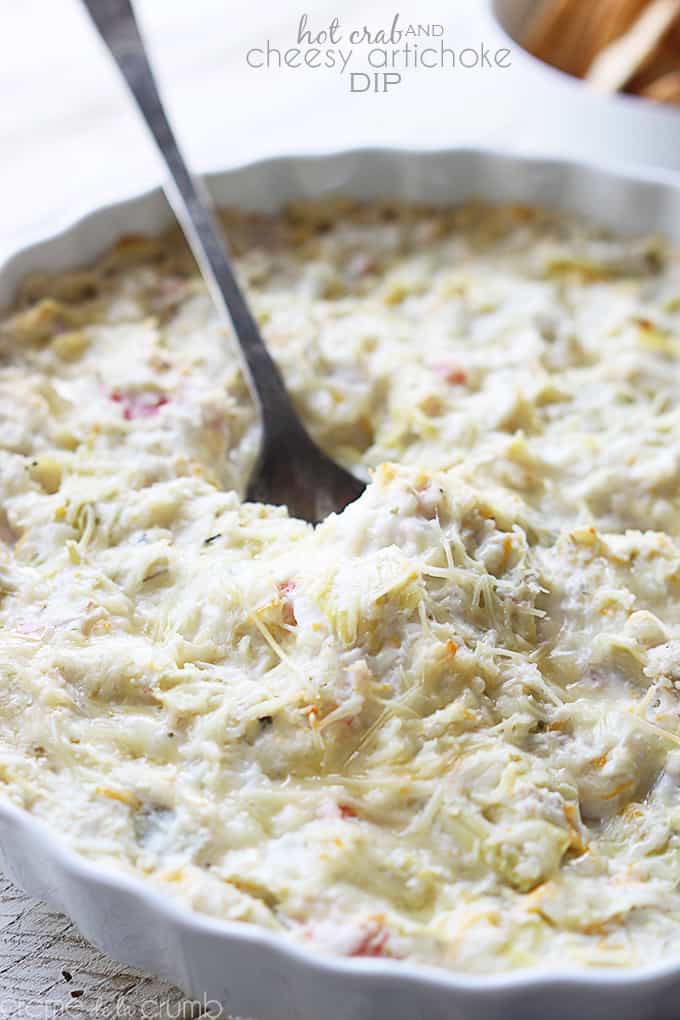 hot crab and cheesy artichoke dip with a spoon in a serving bowl with the title of the recipe in the top middle of the image.