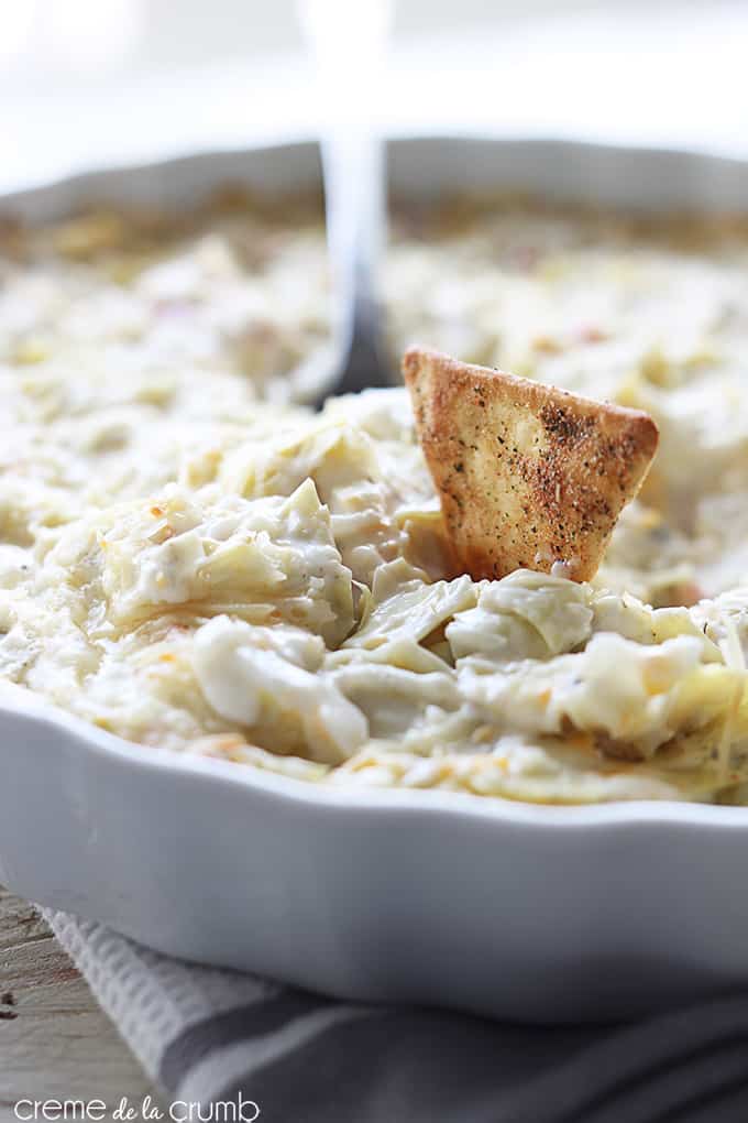 hot crab and cheesy artichoke dip with a spoon and a chip in a serving bowl.