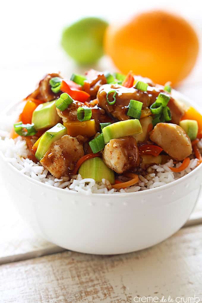 orange teriyaki chicken on rice in a bowl with a whole orange and lime faded in the background.