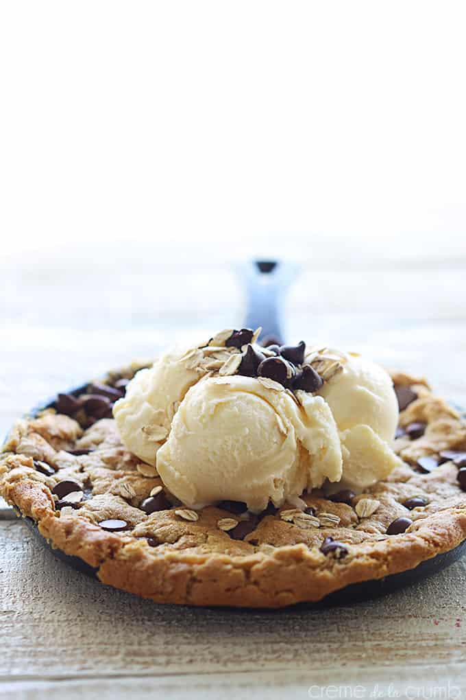 peanut butter oatmeal chocolate chip skillet cookie in a skillet topped with vanilla ice cream, chocolate chips, and oats.