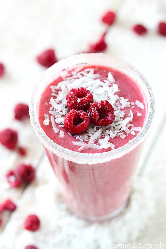 top view of a raspberry coconut smoothie in a tall glass on a wooden table with raspberries and coconut shavings.