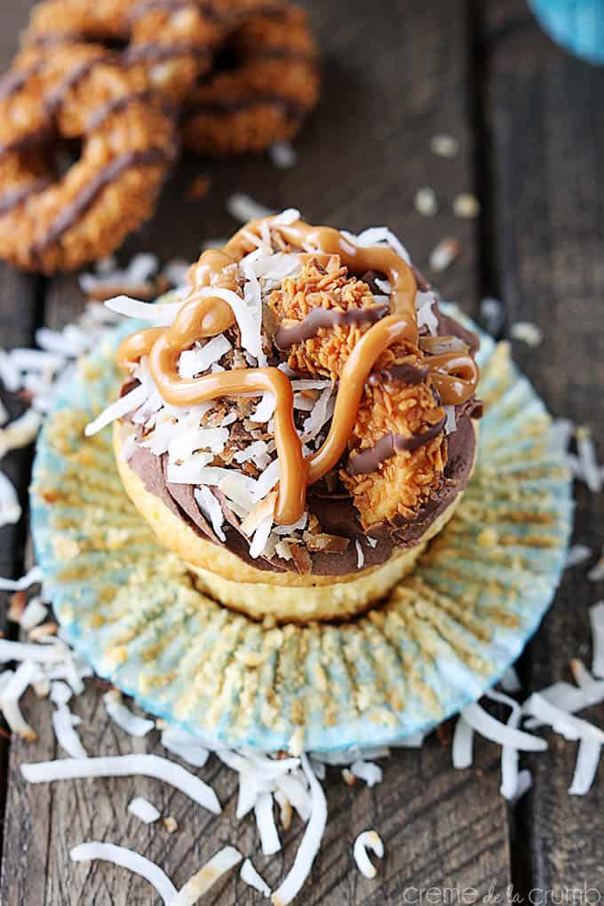 top view of a Samoas cupcake with the cupcake liner opened with coconut shavings surrounding it and Samoas cookies faded on the side.