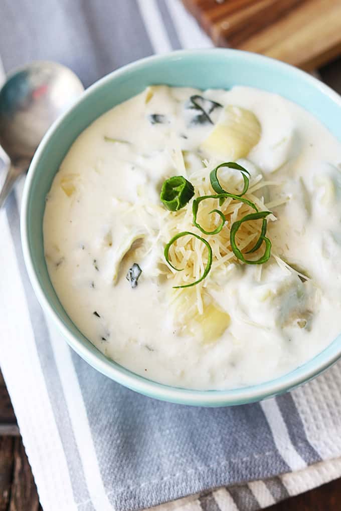 top view of creamy spinach artichoke soup in a bowl on a blue and white cloth napkin with a spoon.