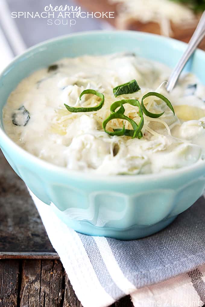 creamy spinach artichoke soup with a spoon in a bowl with the title of the recipe written on the top left corner of the image.