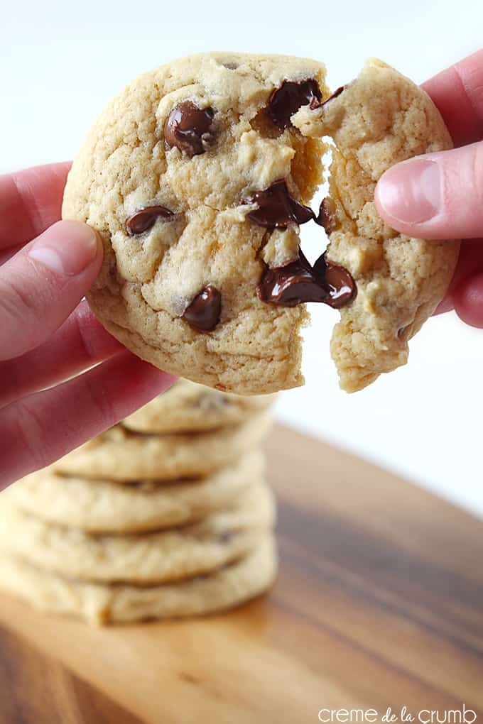 a hand pulling apart a double chewy chocolate chip cookie with more cookies stacked and faded in the background.