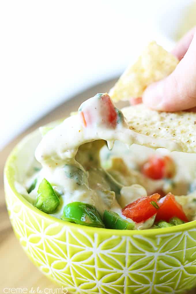 a chip being dipped in green Chile queso blanco in a bowl.