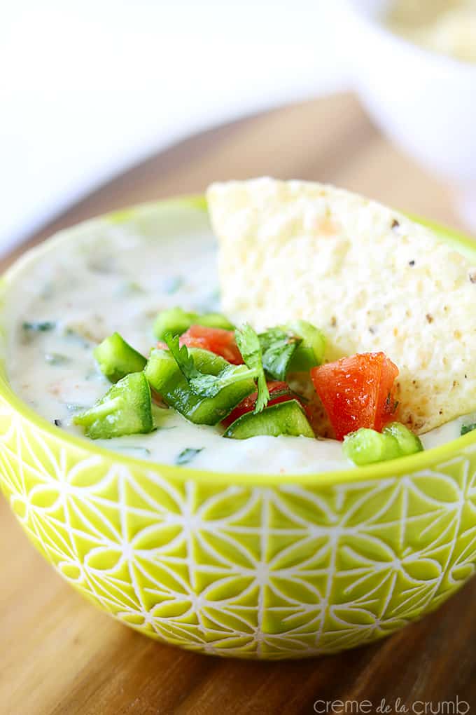 a chip in green Chile queso blanco in a bowl.