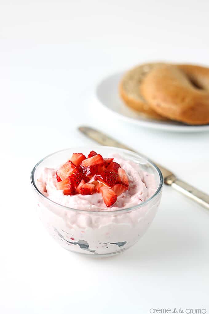 strawberry cream cheese shmear with chopped strawberries on top with a knife on the side and a bagel on a plate faded in the background.