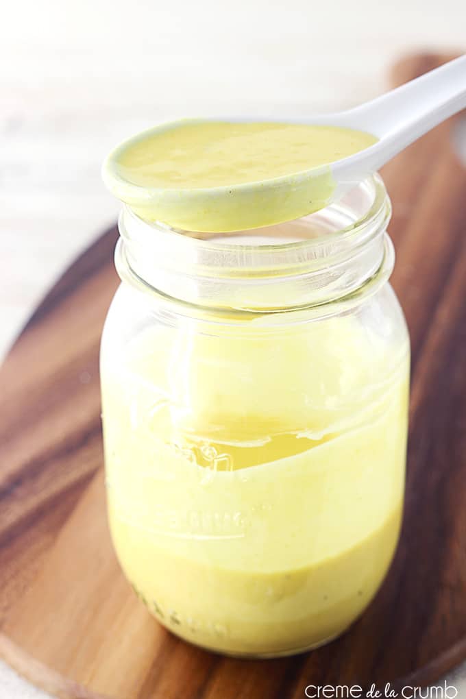 a spoon full of creamy honey mustard dressing sitting on top of a mason jar holding more dressing.