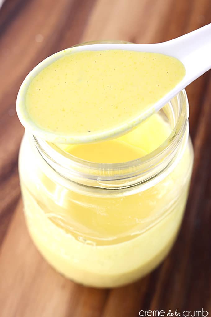 top view of a spoon full of creamy honey mustard dressing on top of a mason jar holding more dressing.