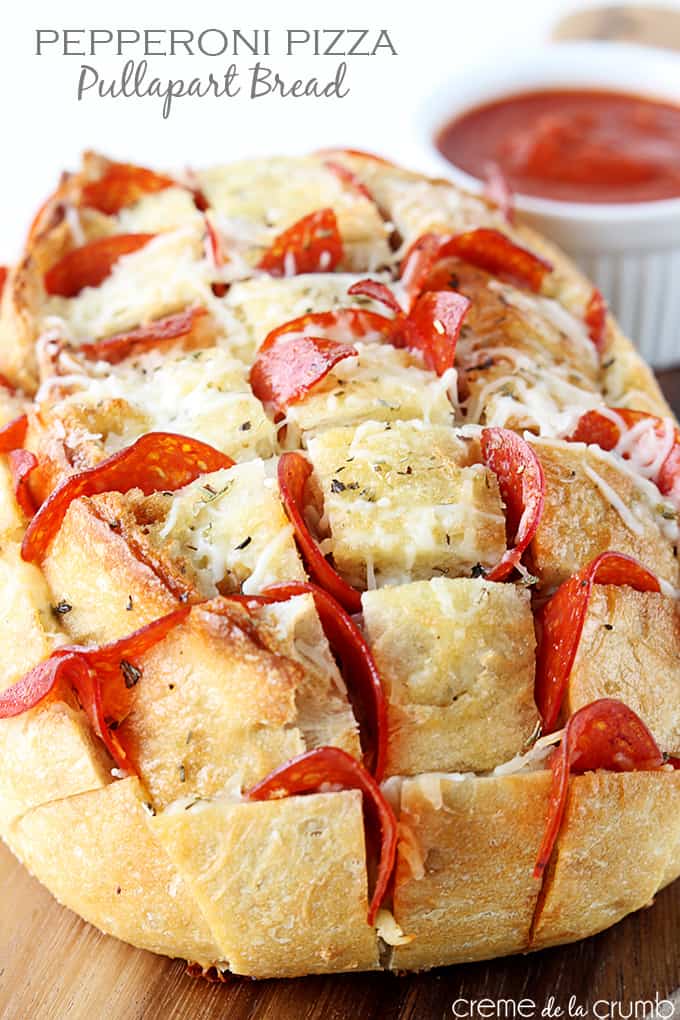 pepperoni pizza pull-apart bread with tomato sauce in a bowl faded in the background with the title of the recipe written on the top left corner of the image.