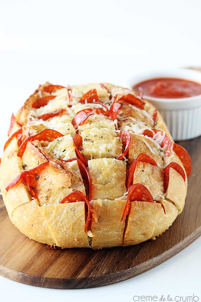 pepperoni pizza pull-apart bread with tomato sauce in a small bowl on a wooden cutting board.
