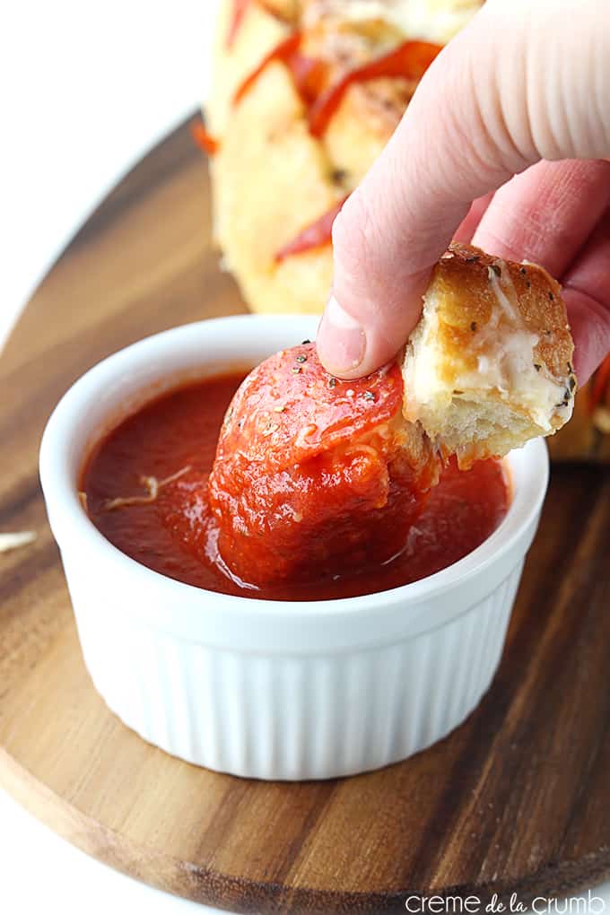 a hand dipping a piece of pepperoni pizza pull-apart bread in tomato sauce.