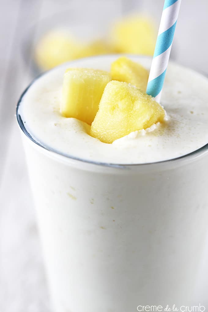 close up of skinny pineapple smoothie in a glass with pineapple chunks and a straw.
