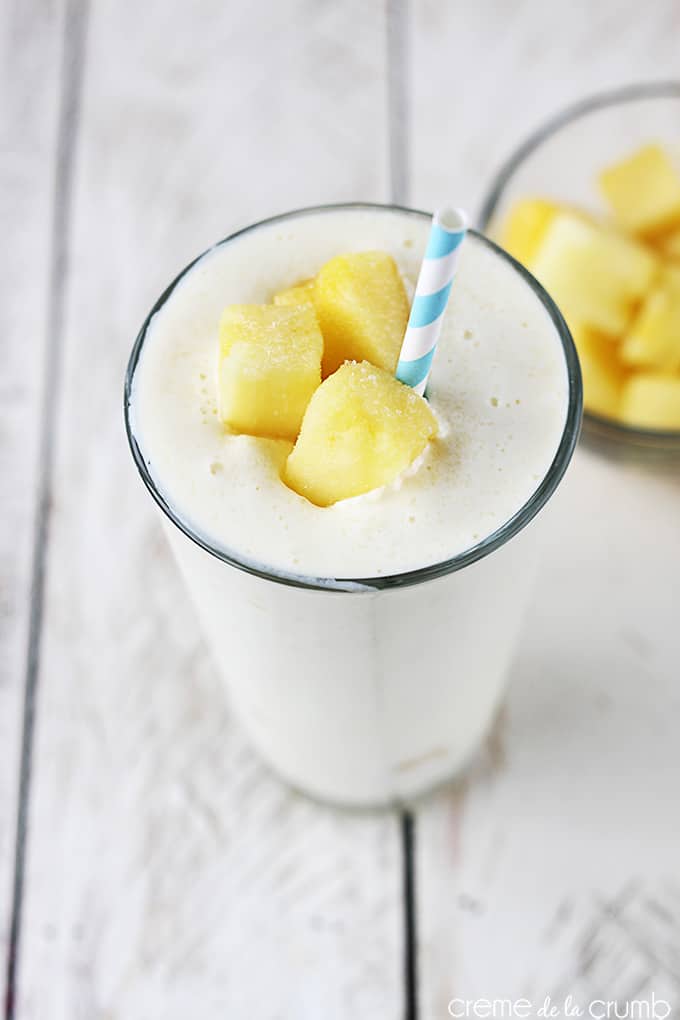 top view of skinny pineapple smoothie in a glass with pineapple chunks and a straw with more pineapple chunks in a glass bowl faded in the background.