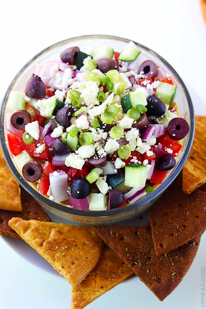 top view of 7 layer Greek hummus in a bowl with pita chips on the side.