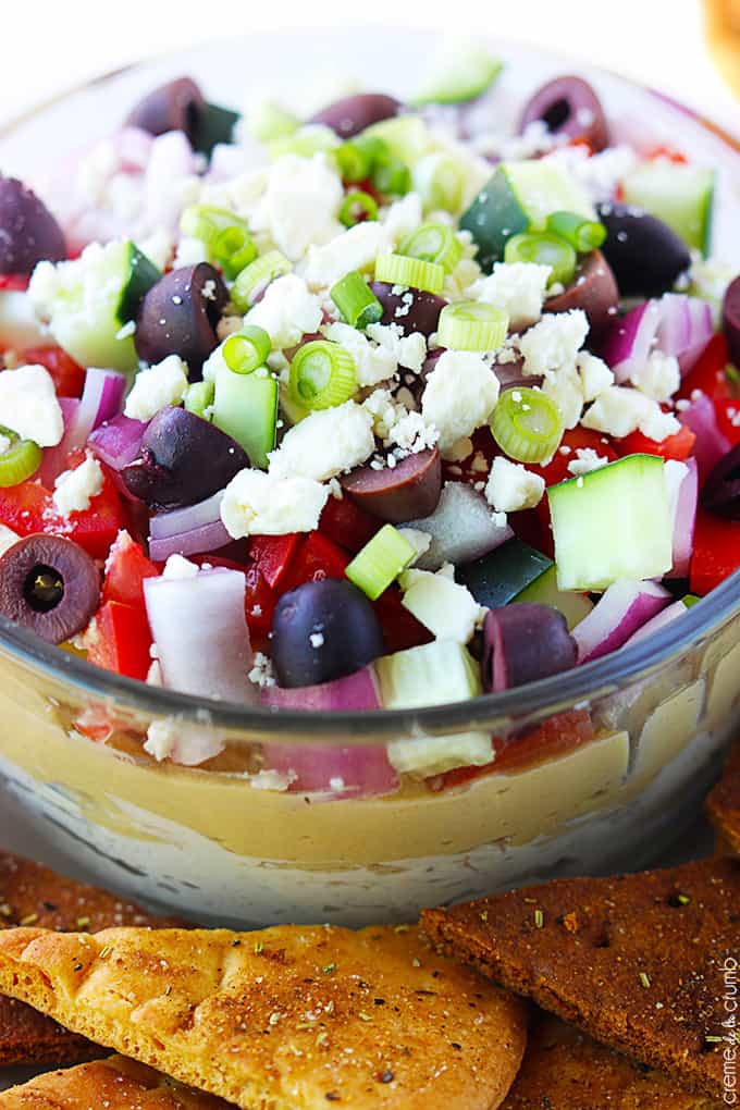 close up of 7 layer Greek hummus in a bowl with pita chips on the side.