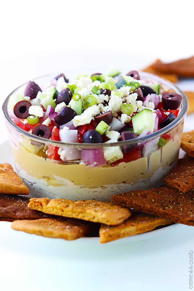 7 layer Greek hummus in a bowl with pita chips on the side.