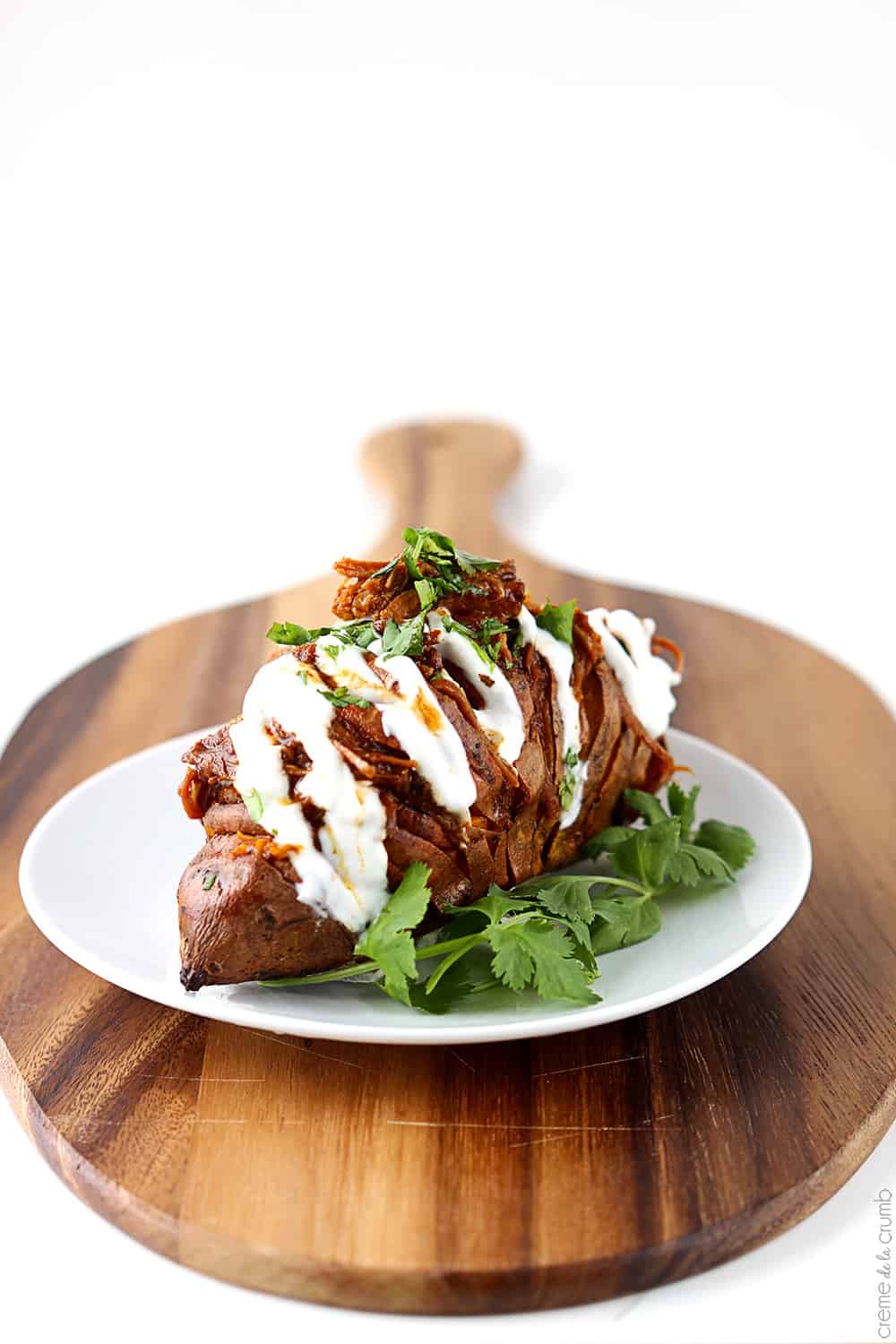 a bbq pulled pork stuffed hasselback sweet potato on a plate on a wooden cutting board.