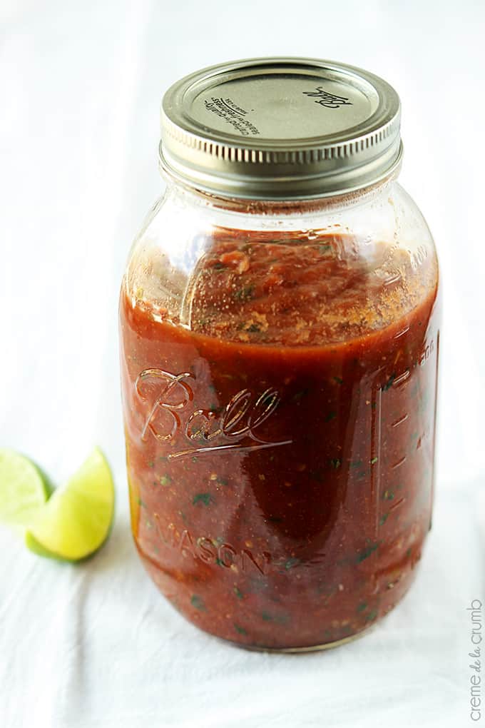 a mason jar of blender salsa with slices of limes on the side.