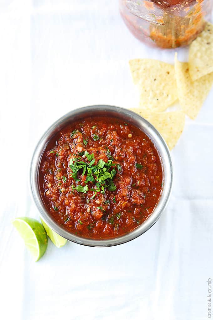 top view of blender salsa in a metal bowl with slices of limes and chips on the side.