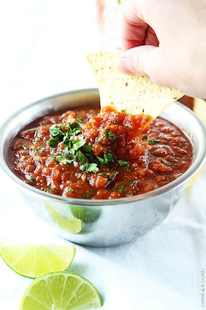 a hand dipping a chip in a bowl of blender salsa with slices of limes on the side.