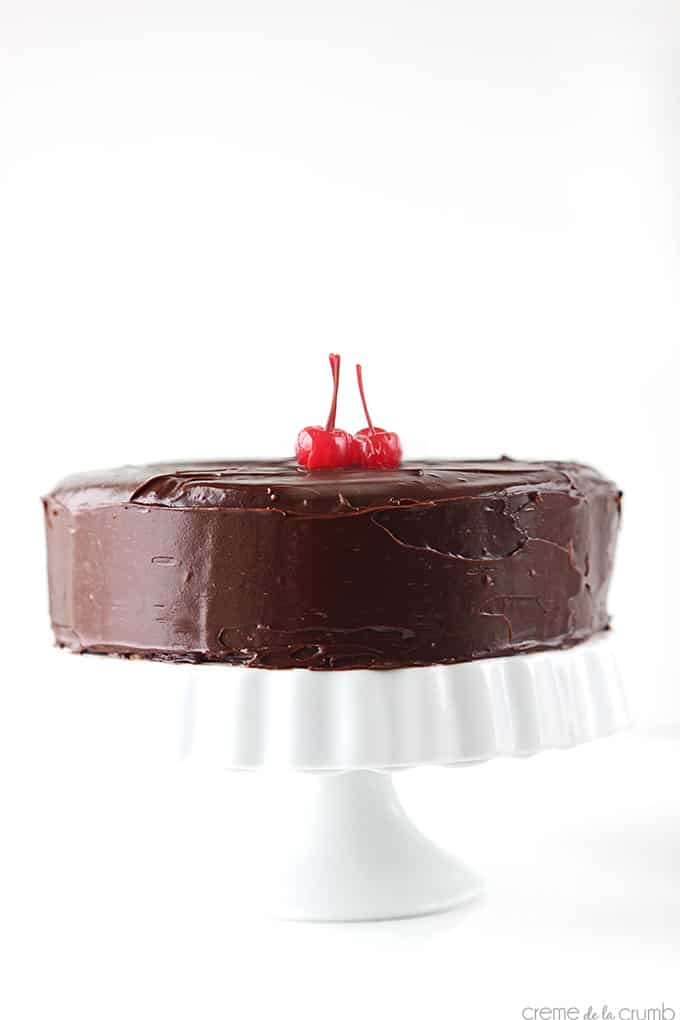 cherry chip cake with chocolate ganache frosting on a cake stand topped with two cherries.