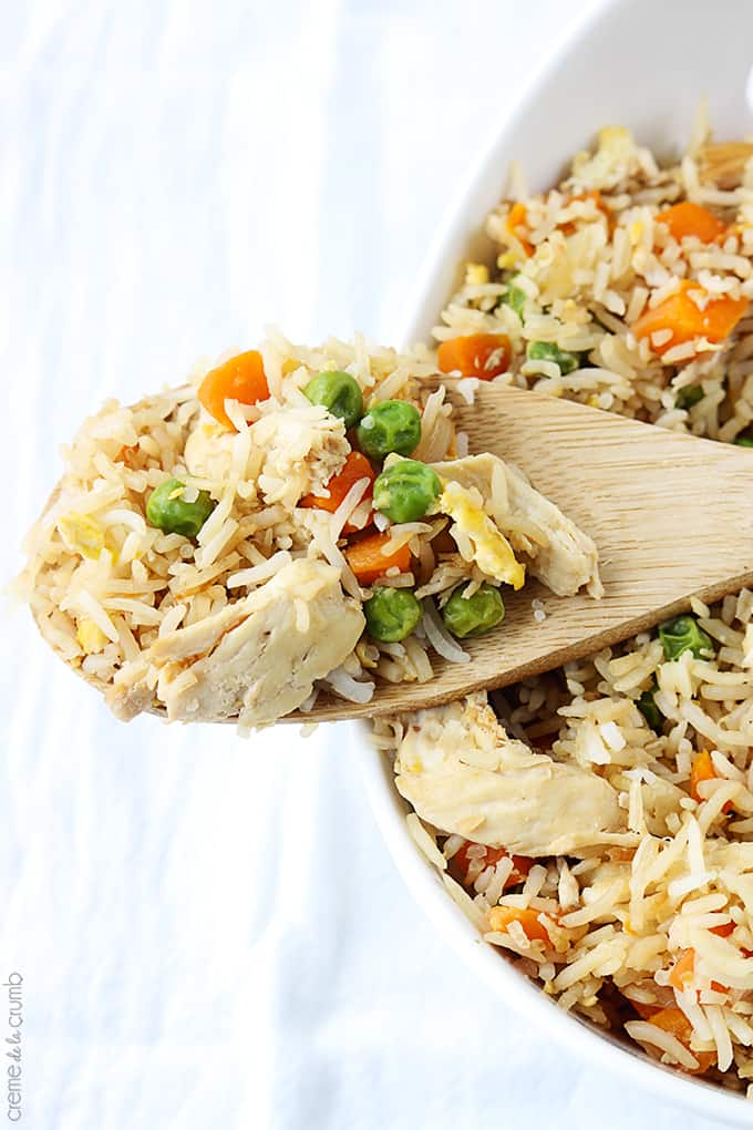 chicken fried rice in a serving tray with a wooden spoon on top with a scoop of rice.