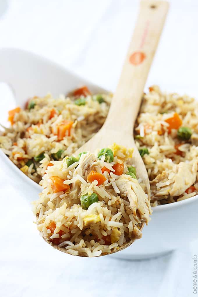 close up of chicken fried rice in a serving tray with a wooden spoon on top with a scoop of rice.