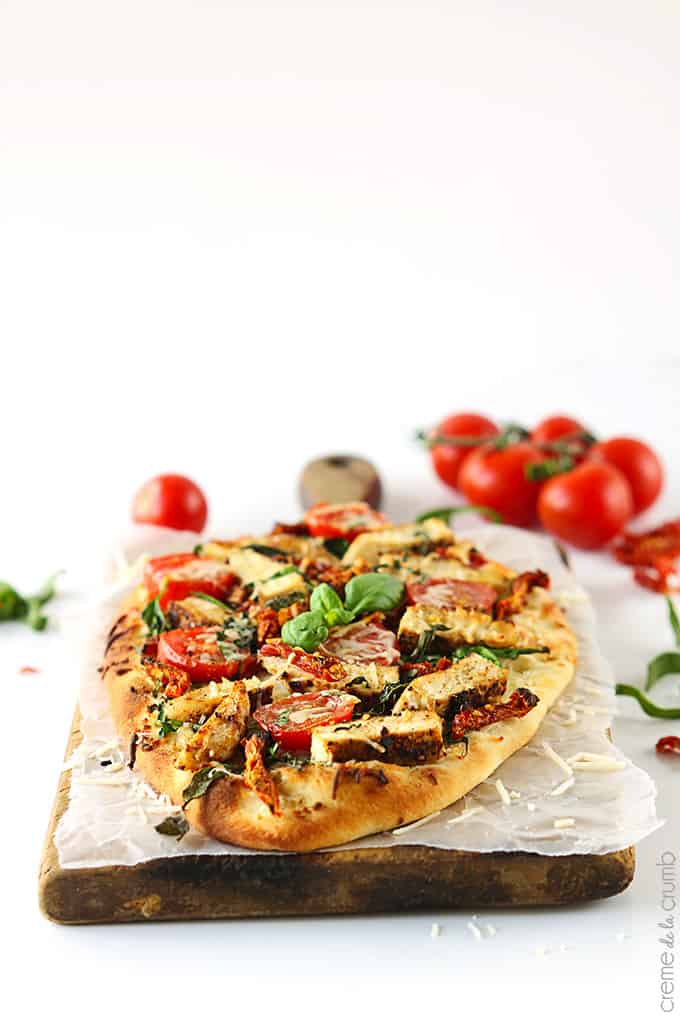 chicken Florentine flat bread pizza with tomatoes faded in the background.