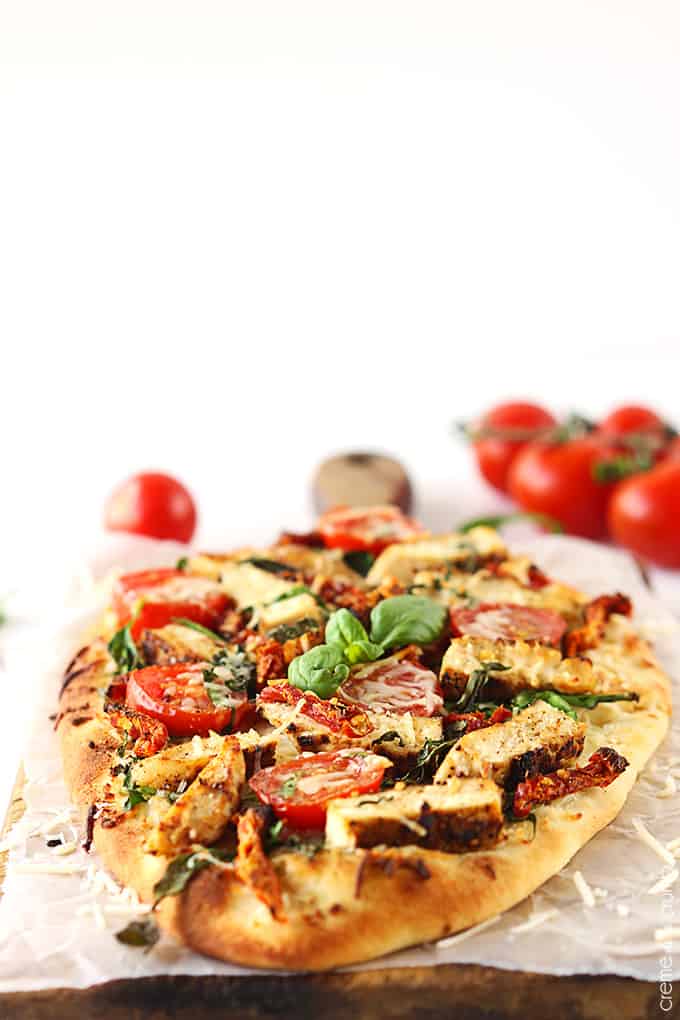 chicken Florentine flat bread pizza with tomatoes faded in the background.