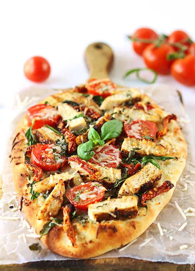 chicken Florentine flat bread pizza with tomatoes faded in the background.