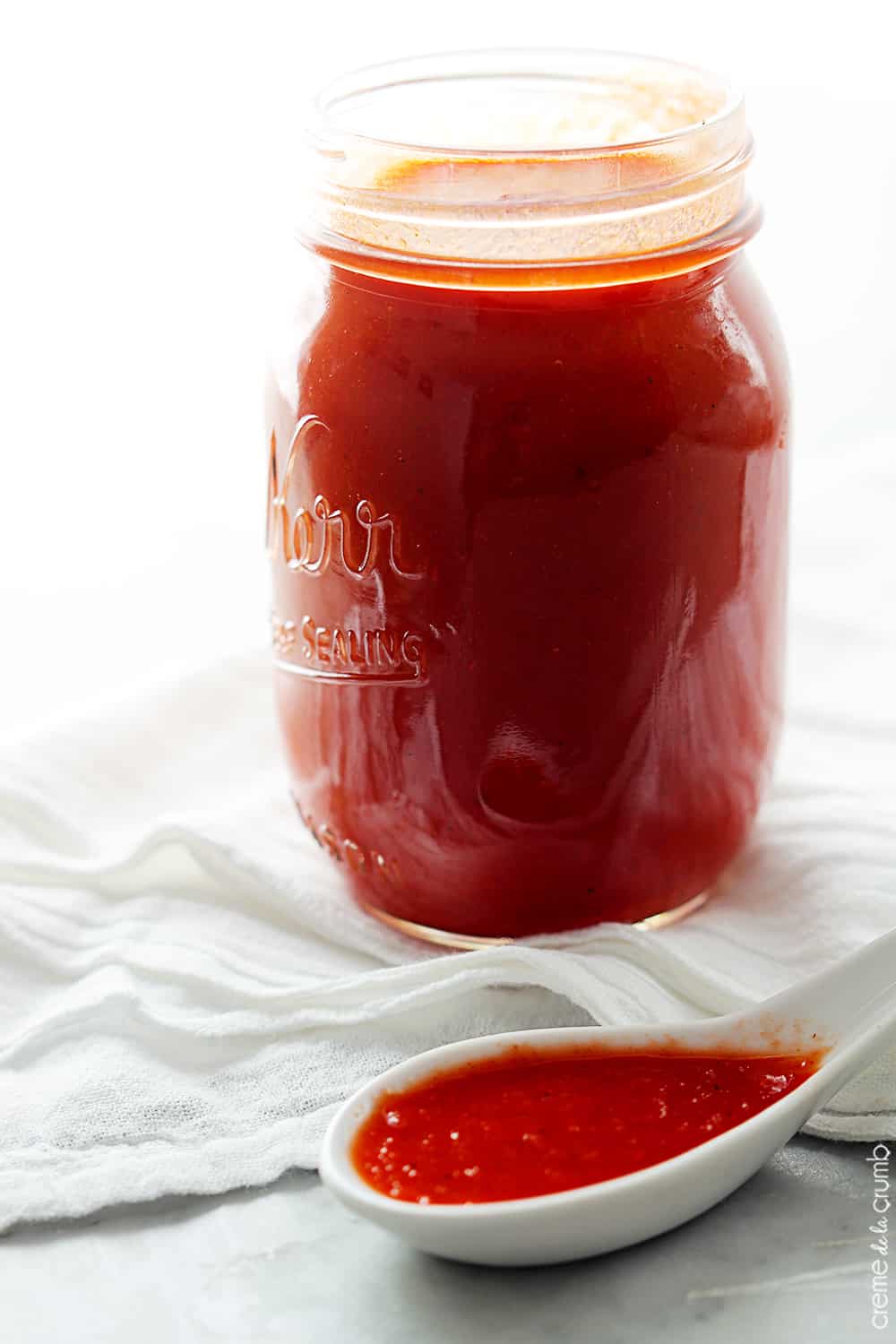 homemade red enchilada sauce in a mason jar with a spoon on the side full of sauce.